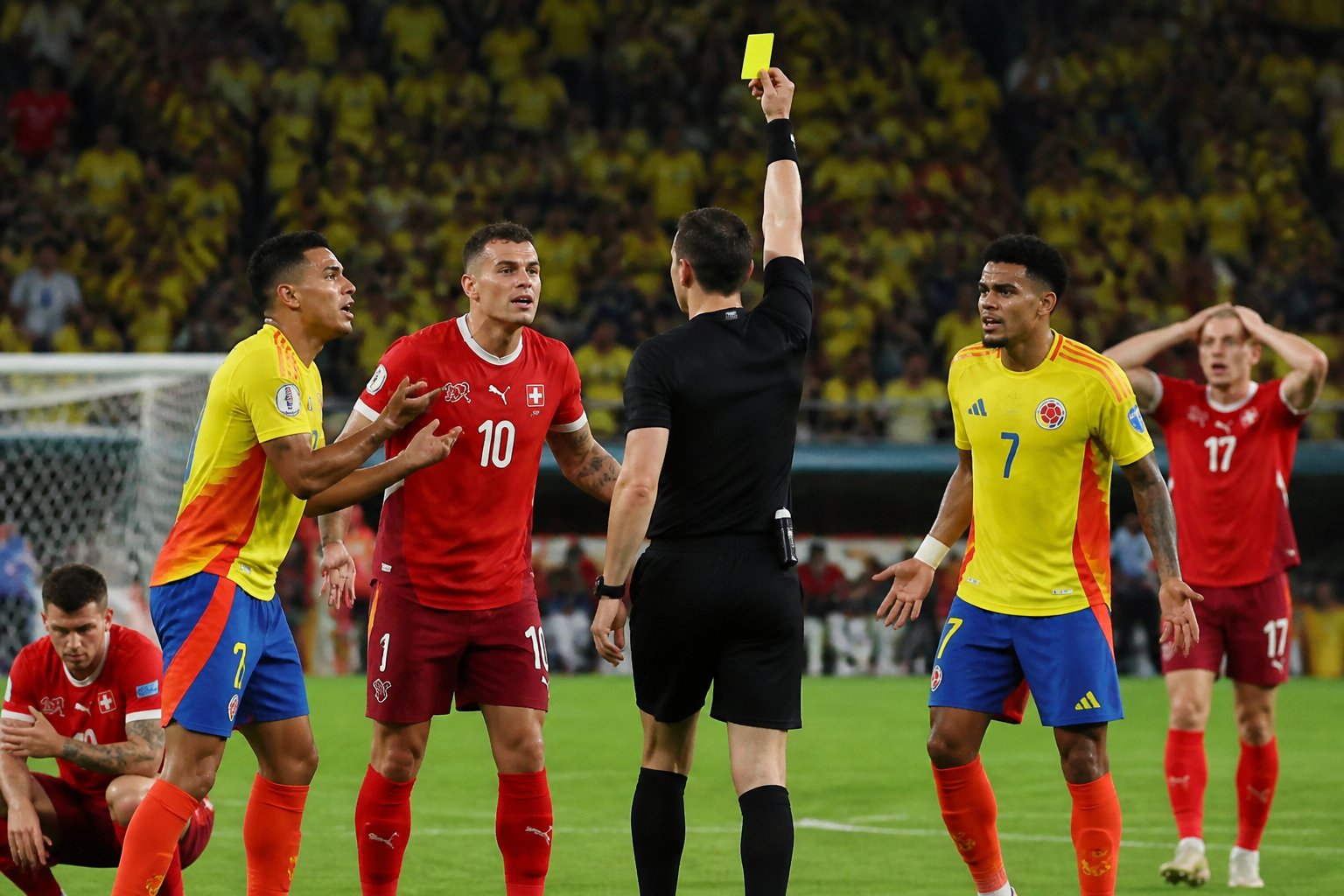 Árbitro tomando una decisión polémica durante un partido de fútbol entre Colombia y Suiza, con jugadores y público reaccionando en el estadio.